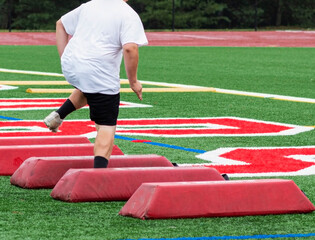 Rear view of teenage football lineman running sideways over barriers
