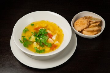 Vegetable soup with chicken and fresh herbs and croutons .On a white plate. On black background