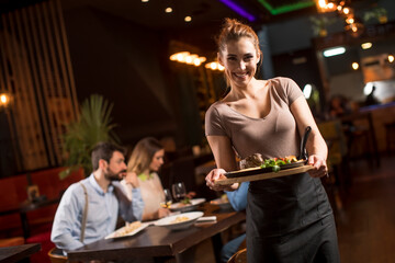 Waiter woman serving group of friends with food in the restaurant
