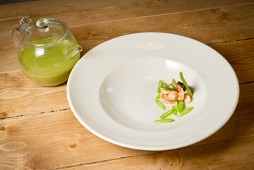 Broccoli cream soup with grilled prawns and asparagus. in white plate.On a rustic wooden table