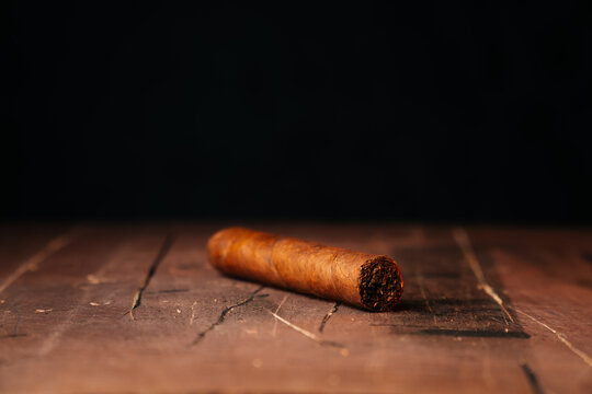 A beautiful fresh Cuban cigar lies alone on the table. Close-up on a dark background