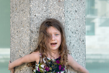 little girl leaning on a concrete column is crying and she is looking scared