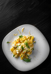 Potato salad with onions and cucumber, mayonnaise-cream dressing in white plate on black wooden table background