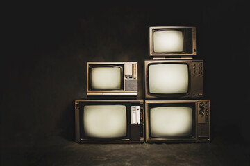 Retro old televisions pile on floor on a dark background, vintage style photo.