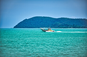 Speed boat on the waves of the azure Andaman sea under the blue sky near the shores of the sandy beautiful exotic and stunning Cenang beach in Langkawi island,