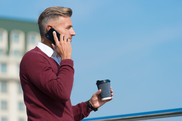 Using communication technologies. Handsome guy talk on phone drinking coffee outdoors. Mobile...