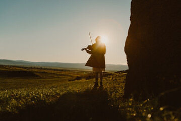 little girl playing on violin outside in the sunset
