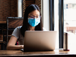 New normal, programmer wearing mask working remotely in cafe during coronavirus era.