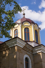 Fototapeta na wymiar Orthodox church with a bell tower. Two crosses on the roof. In the foreground yellow and green bushes and trees 