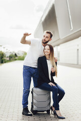 Happy young couple watching airplanes near the airport. A woman sitting on a suitcase. Travel after quarantine. Business trip or vacation trip. A sunny day for airplane flights