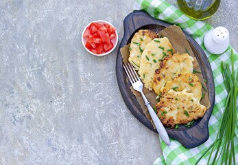 Fritters of fresh young cabbage with chopped tomato and mayonnaise sauce on a wooden plate on a gray concrete background. Vegetarian recipes, recipes from vegetables. Top view, copy space