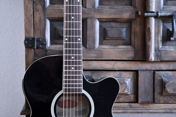 Obraz premium Black acoustic guitar in front of vintage wooden cupboard.