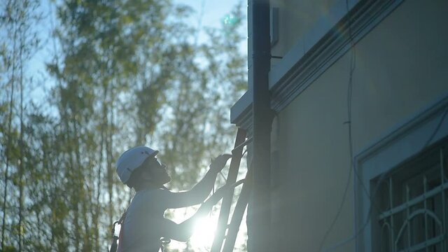 Young apprentice man at work, construction builder climbs up the ladder with safety equipment, white hardhat in construction site
