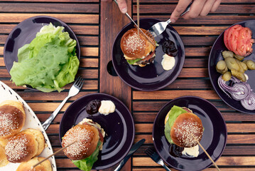 Eating homemade buger with grilled meat and vegetables on a plate with hands. Healty handmade food in a garden outdoors in summer time. Top view and close up. 