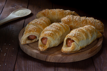 Sausage in dough sprinkled with sesame seeds on a wooden table