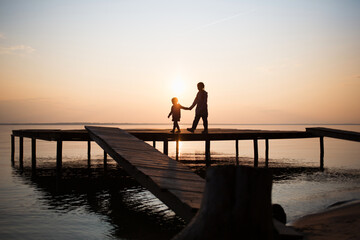 silhouettes of people children on shore lake. Summer sunset on water. evening walk outdoor on bridge