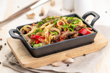 Roast meat with vegetables in a cast iron skillet on a wooden background and a linen napkin.