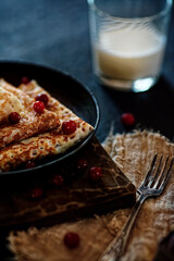 Delicious home-cooked food. Pancakes in a frying pan with cranberry berries and milk. National Russian cuisine. Rustic style