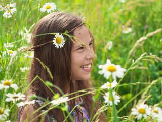 Portrait of a smiling teenager girl among meadow flowers. Happy child in nature.