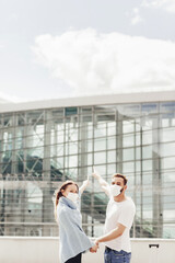 Portrait of happy man and woman in protective masks after coronavirus quarantine, they point to the airport. Young couple near airport, opening air travel, travel concept