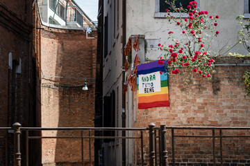 lgbt flag and the italian saying "andra tutto bene" which means "everything will be ok",hanged on a wall near to some beautiful roses during the coronavirus quarantine in Venice Italy 