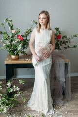 A beautiful girl with blonde hair in a wedding dress holding a bouquet of flowers. Wedding photo session of the bride in the Studio decorated with flowers