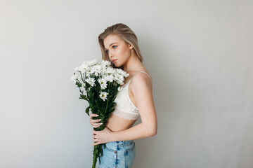 A beautiful girl with blonde hair in underwear is holding a bouquet of daisies. Blonde and a bunch of daisies for mother's Day