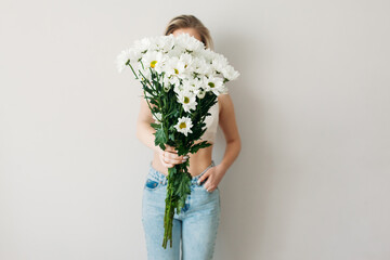 A festive bouquet of daisies in the focus of the lens. A gift for women's day or mother's Day. A beautiful girl with blonde hair in underwear is holding a bouquet of daisies.