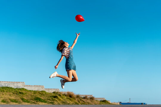 Jumping young woman, letting go of a red ballon