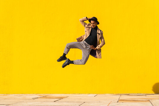 Young man dancing in front of yellow wall, jumping mid air