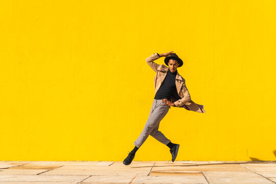 Young man dancing in front of yellow wall, jumping mid air