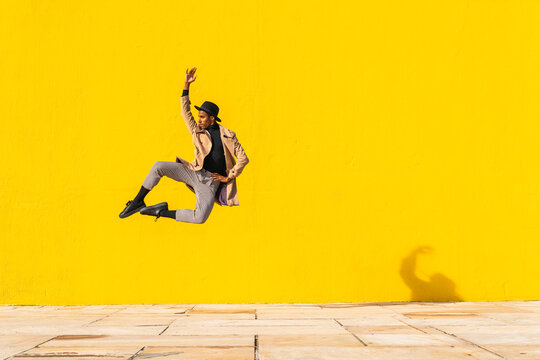 Young man dancing in front of yellow wall, jumping mid air