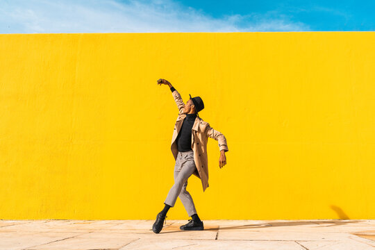 Young man dancing in front of yellow wall, taking selfies