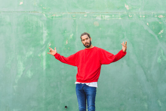 Portrait of angry young man wearing red sweatshirt in front of green wall