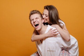 woman bites ear of a young man, woman riding a boyfriend, married couple in home clothes on yellow background, happy relationship, young woman hugs man