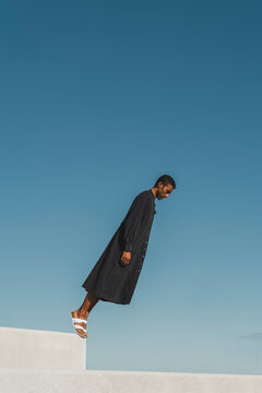 Young man wearing black kaftan standing tilted under blue sky