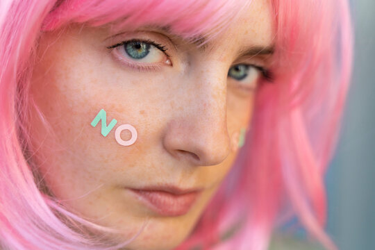 Portrait of young woman wearing pink wig with word 'no' on her cheek