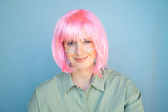 Young woman wearing pink wig, letters on her face, free doom
