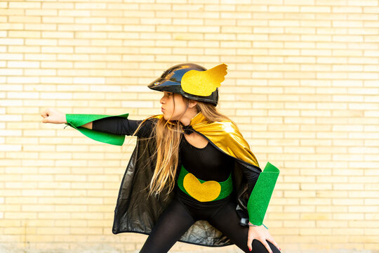 Girl in super heroine costume posing at brick wall