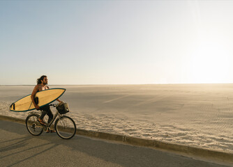 Surfer riding a bicycle during the sunset in the beach, Costa Nova, Portugal