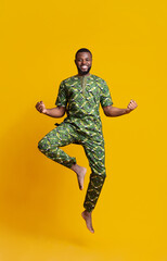 Cheerful african guy celebrating success, jumping up over yellow