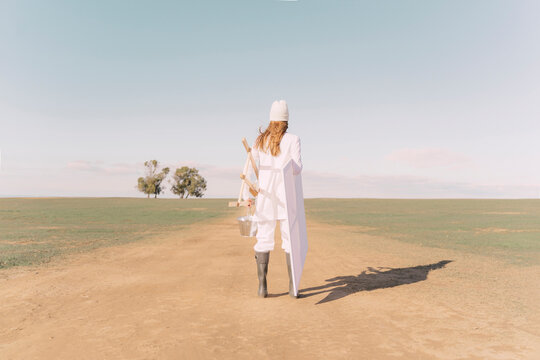 Young woman carrying easel and empty canvas on dry field