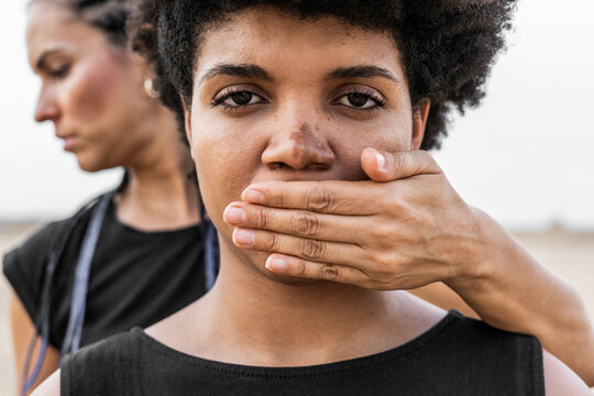 Woman's hand covering mouth of another woman, close-up