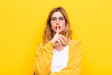 young pretty blonde woman asking for silence and quiet, gesturing with finger in front of mouth,...
