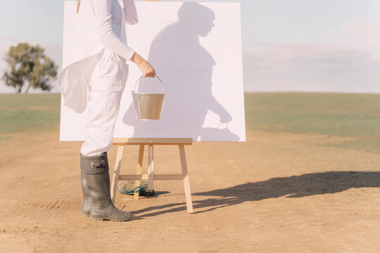 Young woman on dry field, starting to paint on white canvas