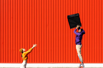 Young man and woman performing with a box in front of a red wall