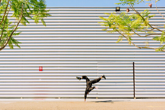 Man wearing black overall doing handstand in front of industrial building