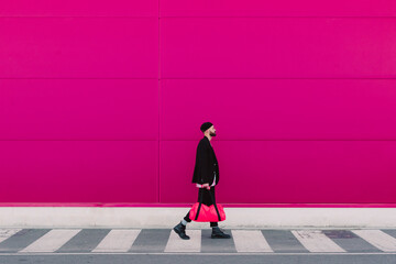 Young man walking with travelling bag in front of a pink wall