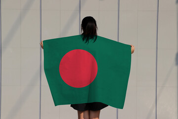 Woman holding Bangladesh flag on her shoulder and turn back on grey background.