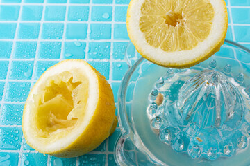 Top view of squeezed lemon, with glass juicer and lemon juice, on light blue ceramic with water...